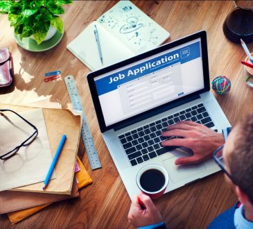 Overhead view of man working on job application on laptop while holding coffee