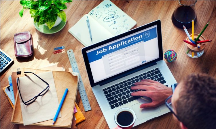Overhead view of man working on job application on laptop while holding coffee