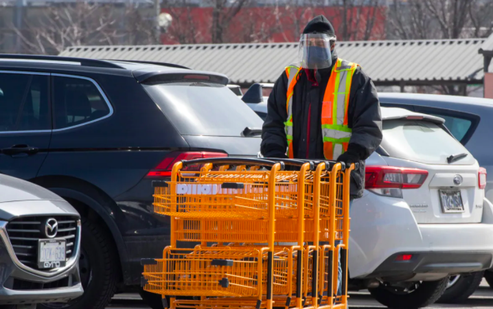 Worker wearing face shield and mask pushing grocery carts in parking lot