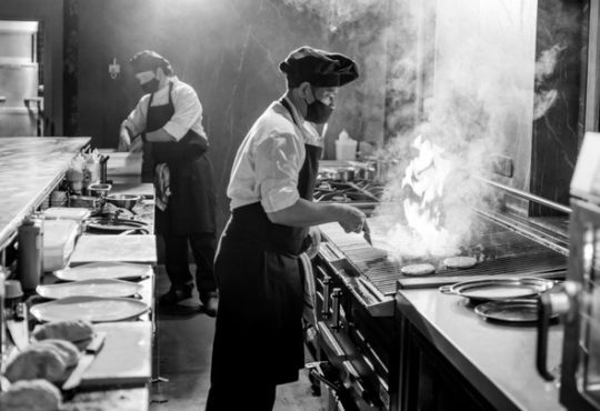 Black and white image of two chefs cooking in restaurant kitchen