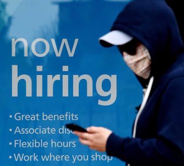 Masked person walking past business window with "now hiring" sign