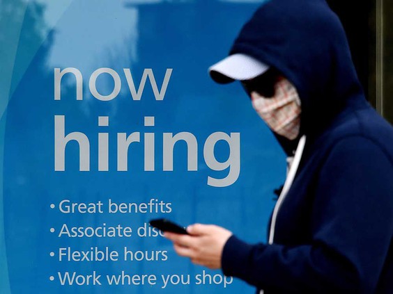 Masked person walking past business window with "now hiring" sign