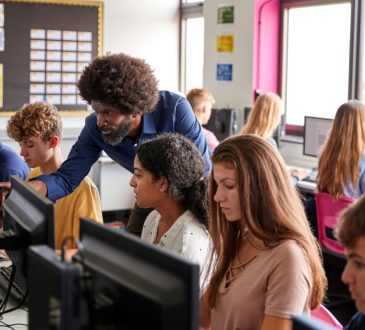 Teacher helps high school students in computer lab.