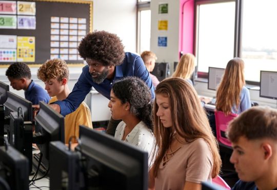 Teacher helps high school students in computer lab.