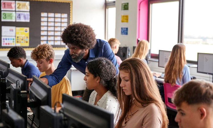 Teacher helps high school students in computer lab.