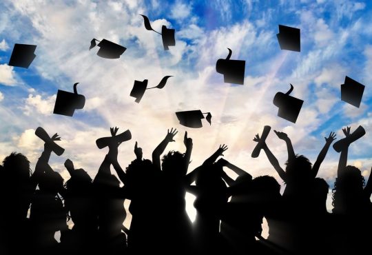 Silhouetted image of group of people throwing graduation caps in the air outside