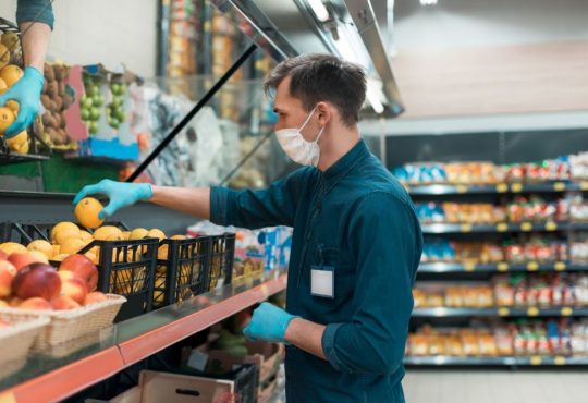 Masked man stocks produce shelf in grocery store