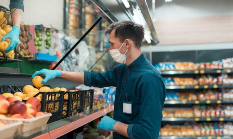 Masked man stocks produce shelf in grocery store