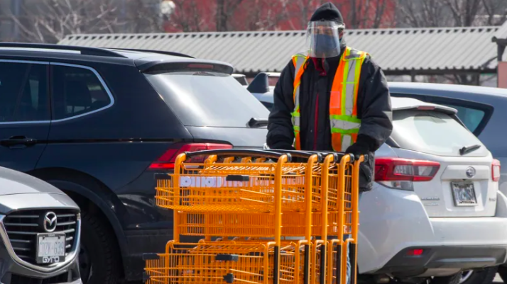 Worker wearing face shield pushing grocery carts in store parking lot