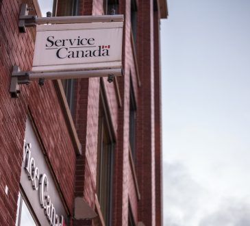 Picture of a Service Canada sign on the exterior of their red brick office building in Toronto