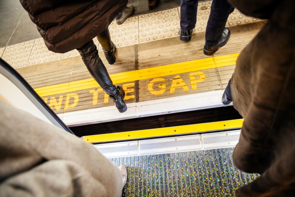 View from above of people walking over "Mind the Gap" writing on floor of London Underground  while exiting the tube