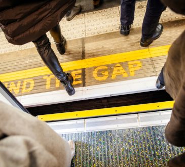 View from above of people walking over "Mind the Gap" writing on floor of London Underground while exiting the tube