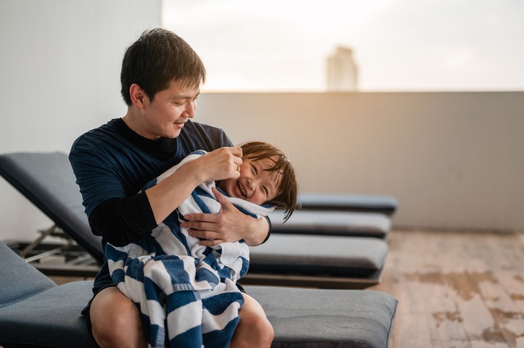 Dad drying off laughing kid with towel after swimming lesson