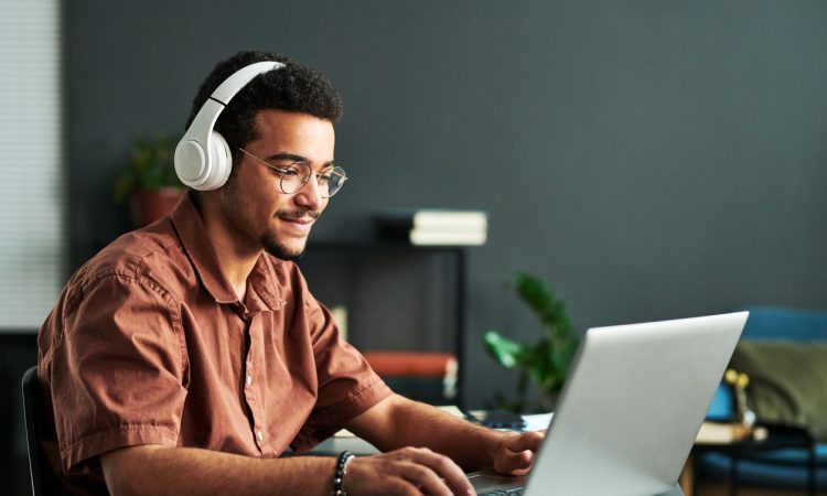 Young smiling man in headphones typing on laptop keyboard