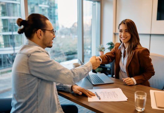 Man and woman shake hands across table during interview.