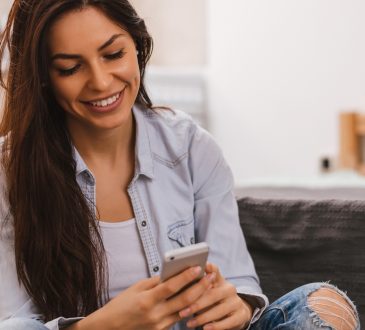 Woman sitting on couch, smiling and looking down at phone