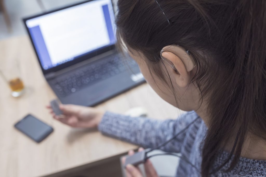 Woman wearing hearing aid working on laptop.