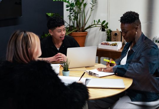 A group of co-workers of various genders having a meeting at a round table in an office.