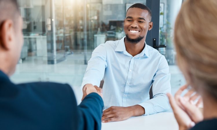 Two men shake hands across table during job interview.