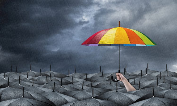 Sea of black umbrellas amid storm with hand holding rainbow umbrella above the rest