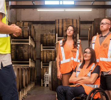 Four people in safety vests in warehouse with large barrels