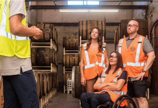 Four people in safety vests in warehouse with large barrels