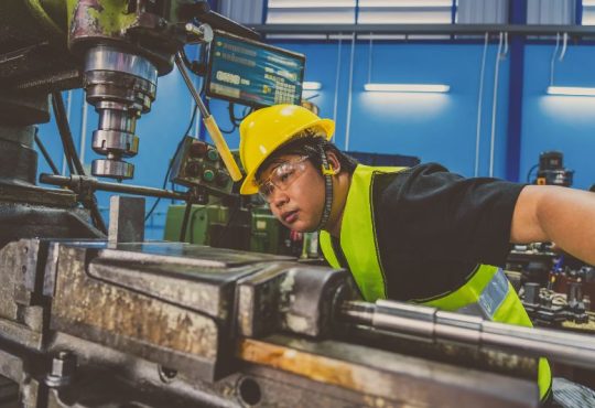 Man working in factory looking closely at piece of machinery