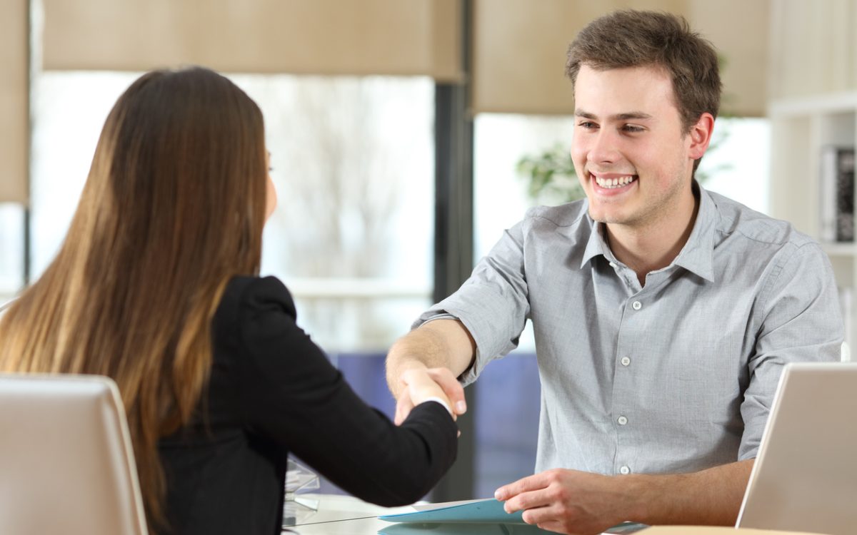 Man and woman shaking hands across desk.