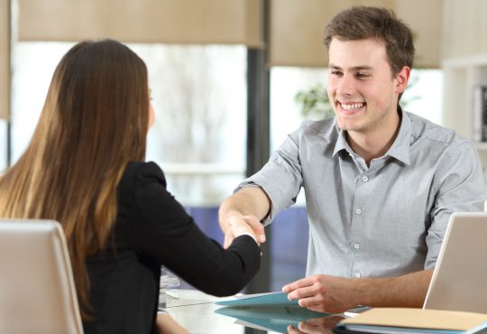 Man and woman shaking hands across desk.