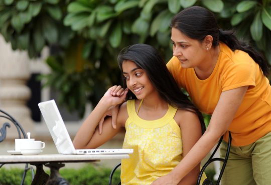 Mom looking over daughter's shoulder at laptop screen.
