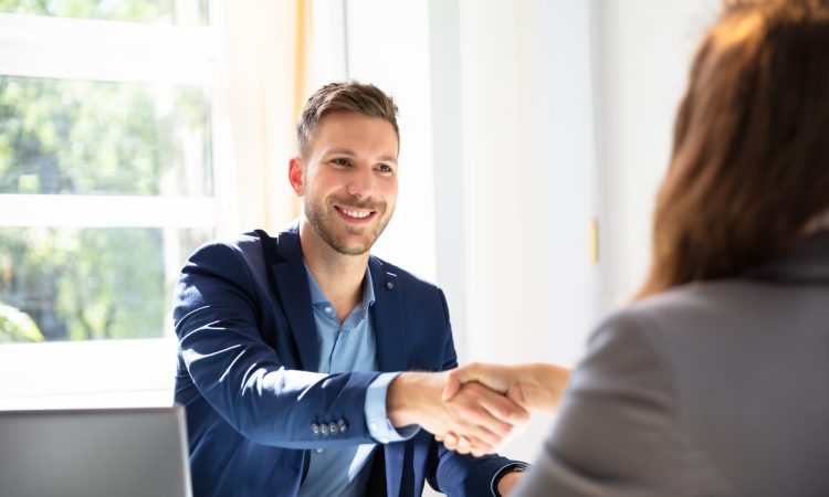 Smiling man shaking hands with interviewer across desk