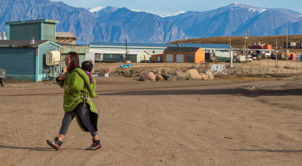 Inuit woman walking with baby in Pond Inlet, Baffin Island.