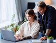 One person standing behind another working on laptop