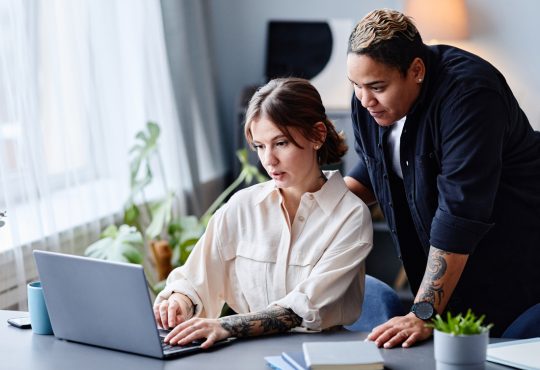 One person standing behind another working on laptop