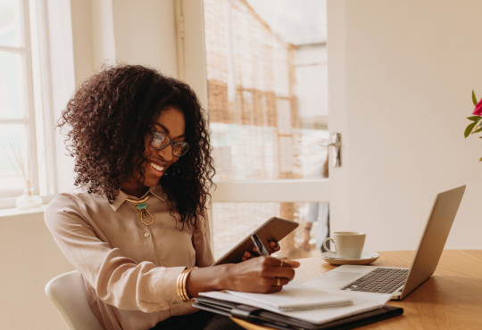 Woman working from home with laptop, notes, and tablet