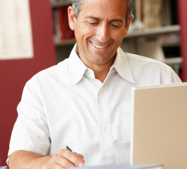 Mature student studying in library with laptop and book