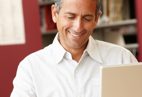 Mature student studying in library with laptop and book