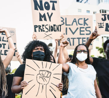 Black Lives Matter protest during the pandemic, with people holding signs reading "not my president" and "black lives matter."