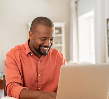 Man in orange-red shirt using laptop and smiling