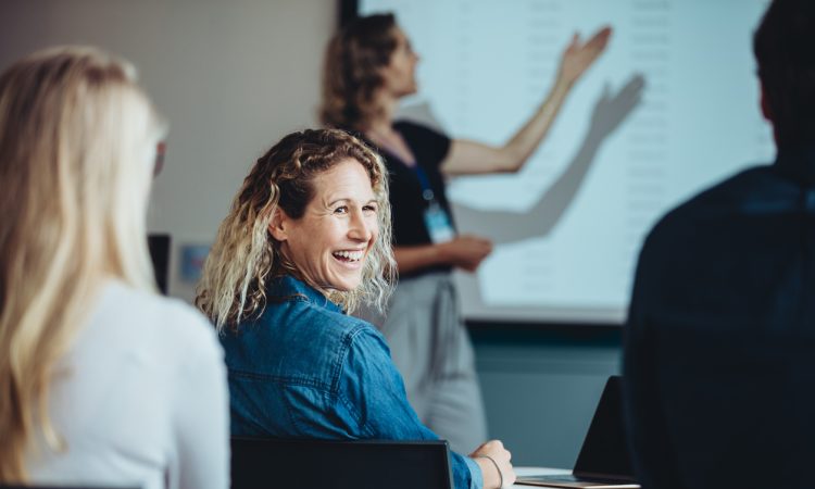 Rear view of a woman sitting in audience looking back at a colleague and smiling during a conference.