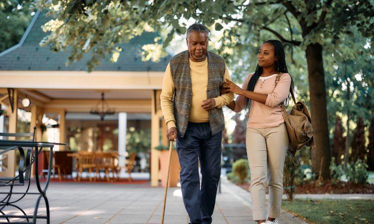 Young woman supporting arm of older man walking with cane