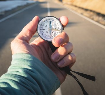 Close-up of hand holding compass against backdrop of mountain road