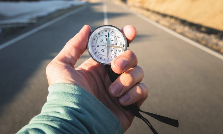 Close-up of hand holding compass against backdrop of mountain road