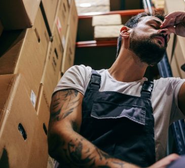 Stressed man at work, crouching down between boxes in back room