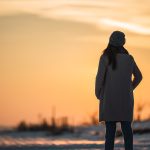 Woman pictured from behind standing outside looking at snowy landscape at dusk