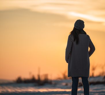 Woman pictured from behind standing outside looking at snowy landscape at dusk