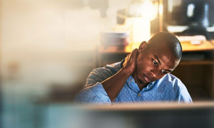 Man sitting at computer in office rubbing neck