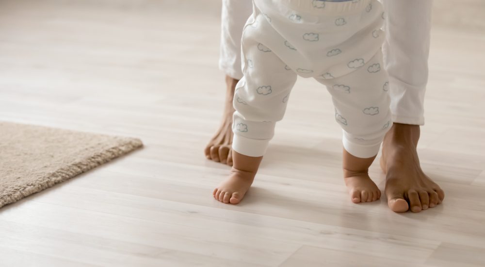 Photo of toddler trying to walk with mom behind, seen from waist down