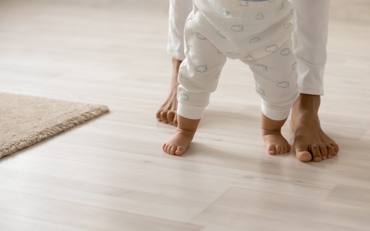 Photo of toddler trying to walk with mom behind, seen from waist down