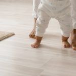 Photo of toddler trying to walk with mom behind, seen from waist down